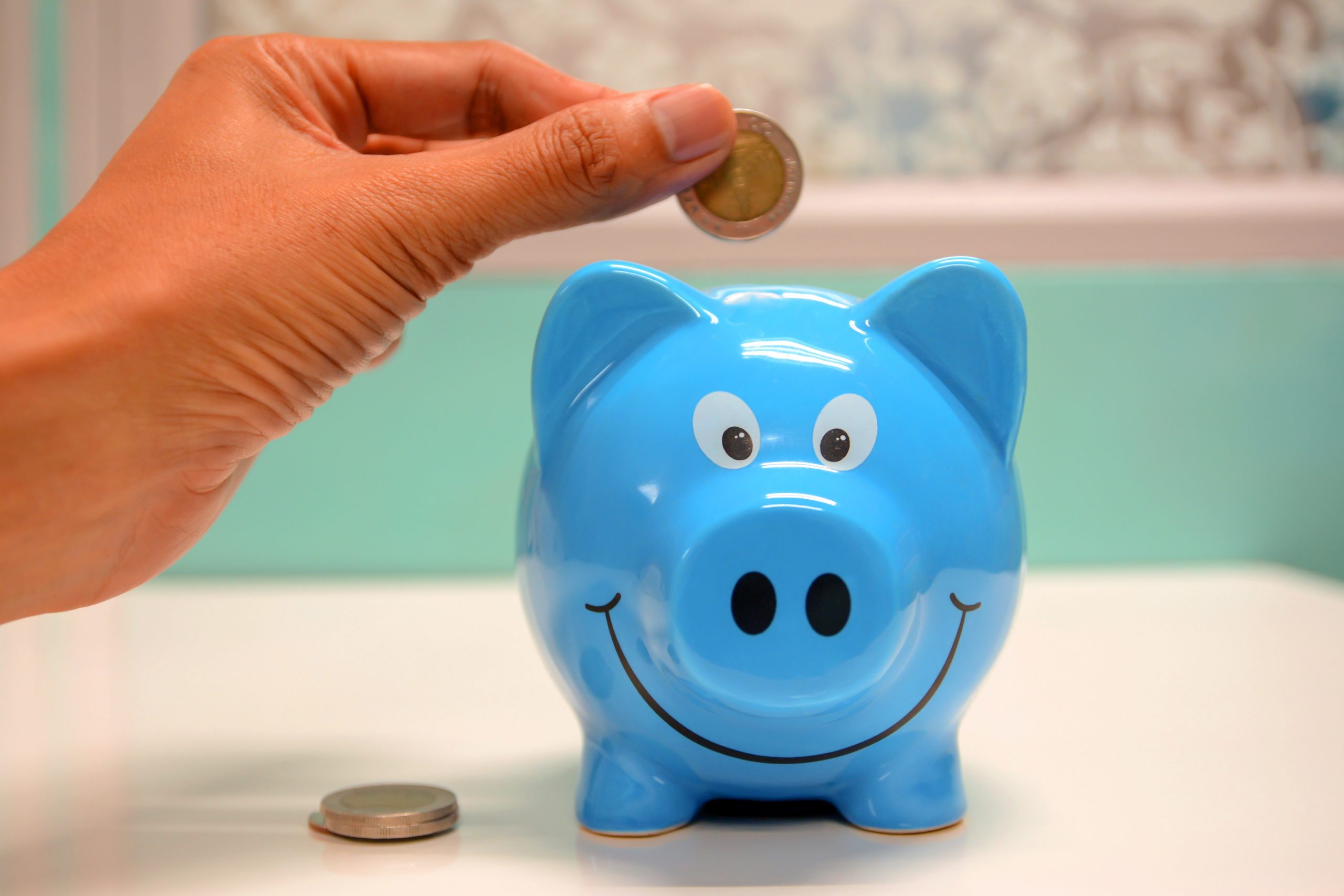 Blue piggy bank, a hand putting one pound coin in to illustrate the south west fund