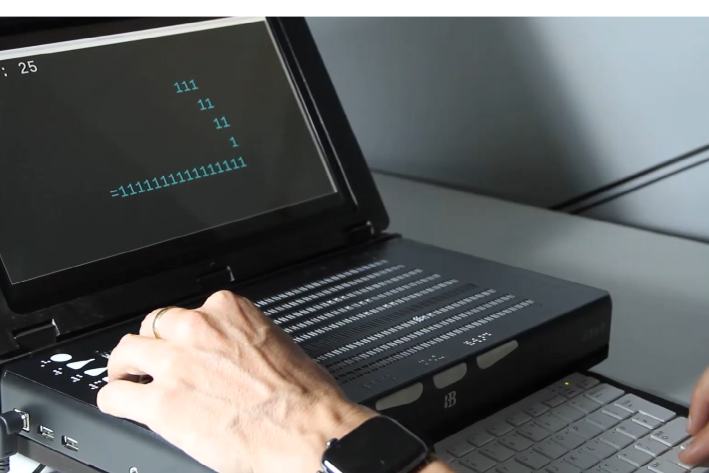 Image of the Canute Dock - a Braille gaming device developed by Bristol Braille Technology. The device has a screen with a black boarder and a braille touchpad, a pair of white hands are interacting with the device.