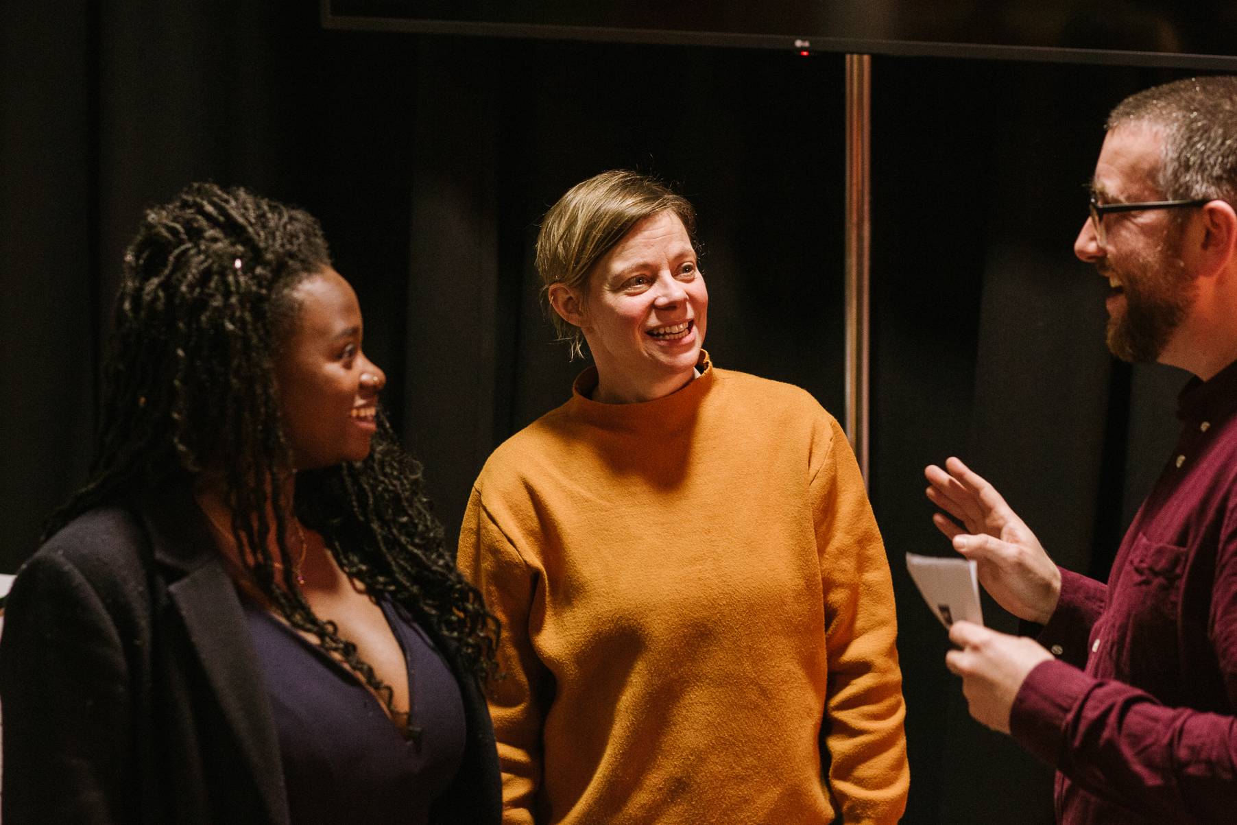 A black woman stood next to an older white woman are both facing a white man who is speaking - they are all smiling