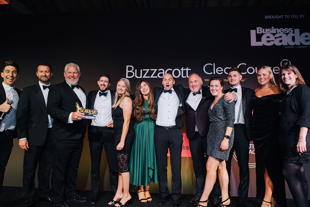 The Xledger UK team stands in a row dressed in black tie at the Business Leader awards show, accepting their award for Scale Up of the Year.