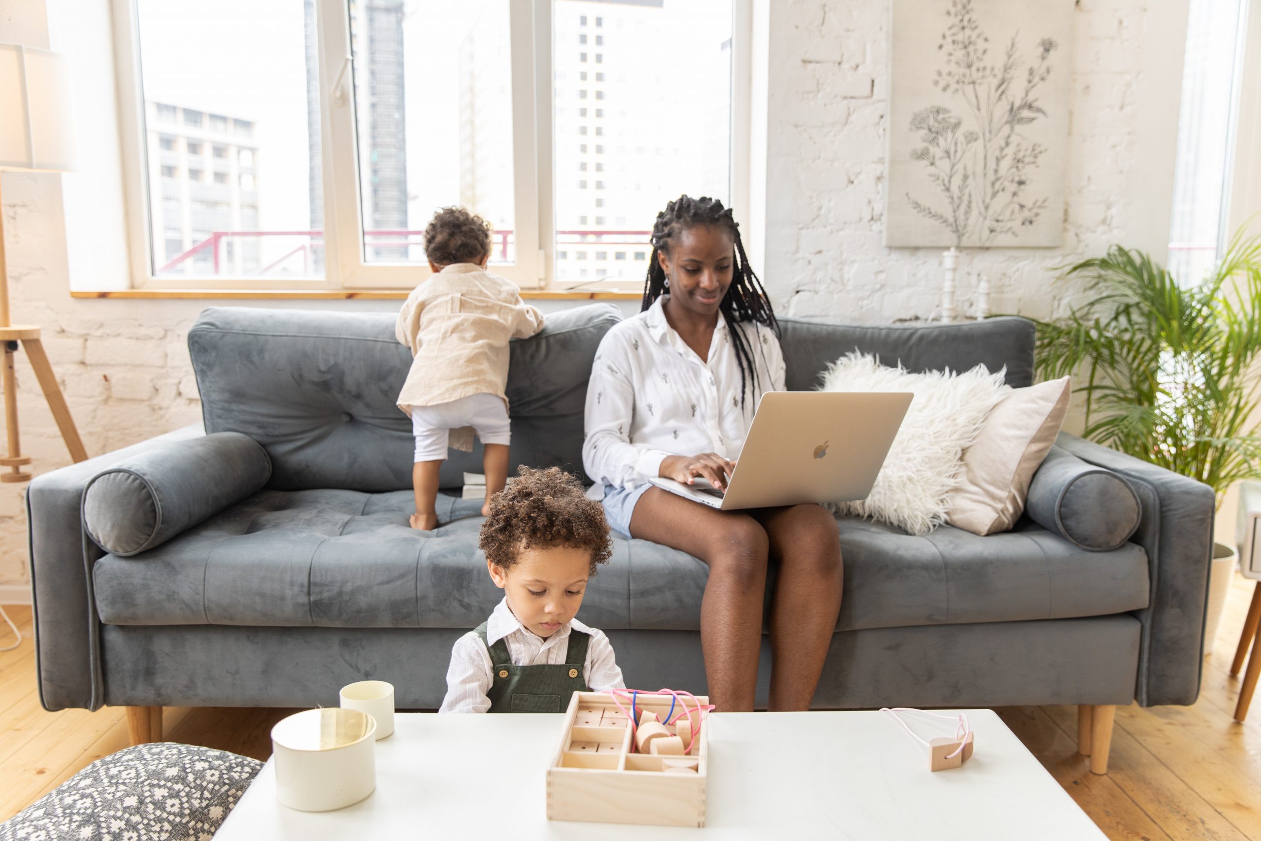 A black woman on the sofa with a laptop and two kids around her