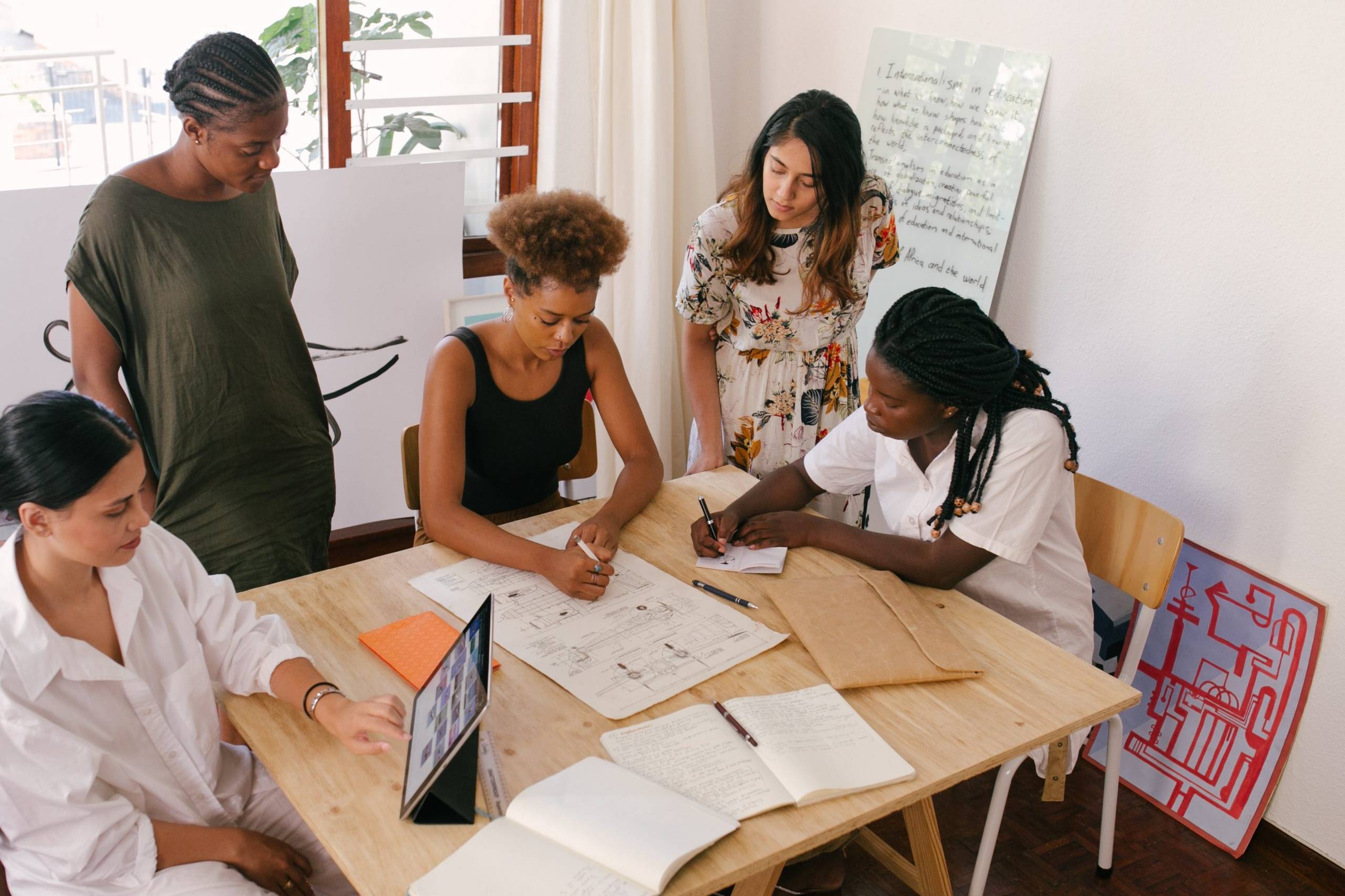 A group of women with different ethnicities sat at a table working over sheets of paper.