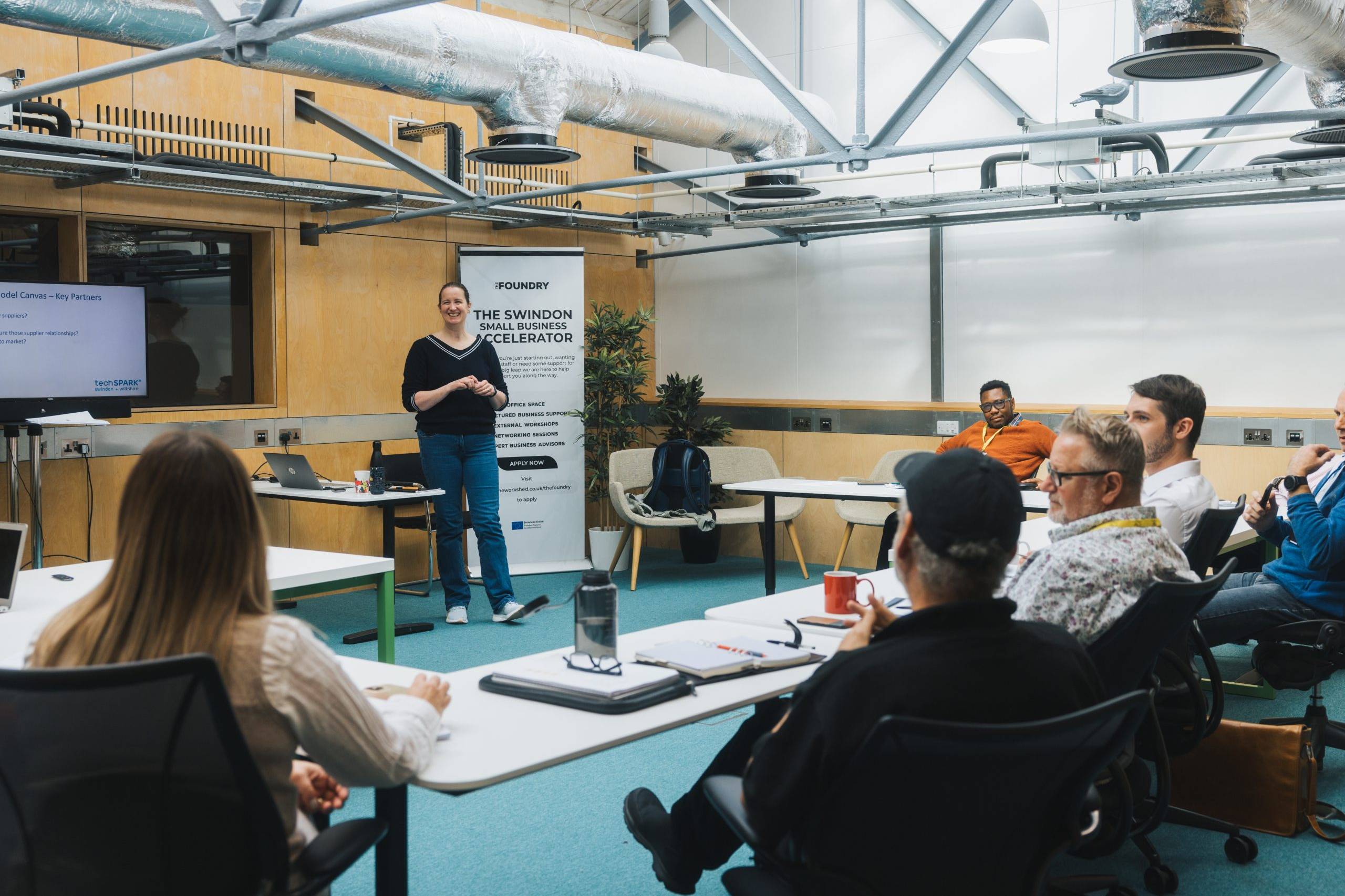 A white woman stands at the from of a room presenting to a group of business owners