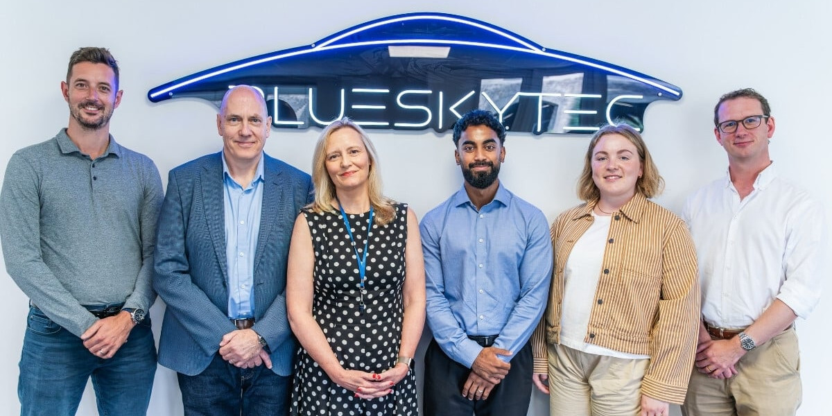 Group photo of six Blueskytec team members and partners standing in front of a neon Blueskytec sign after securing £1.5m investment.