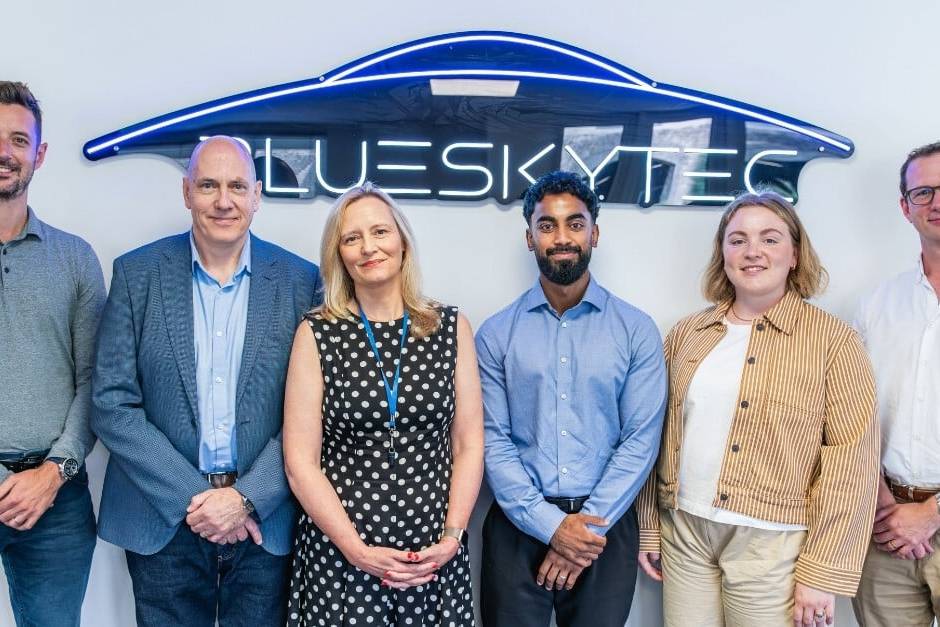 Group photo of six Blueskytec team members and partners standing in front of a neon Blueskytec sign after securing £1.5m investment.